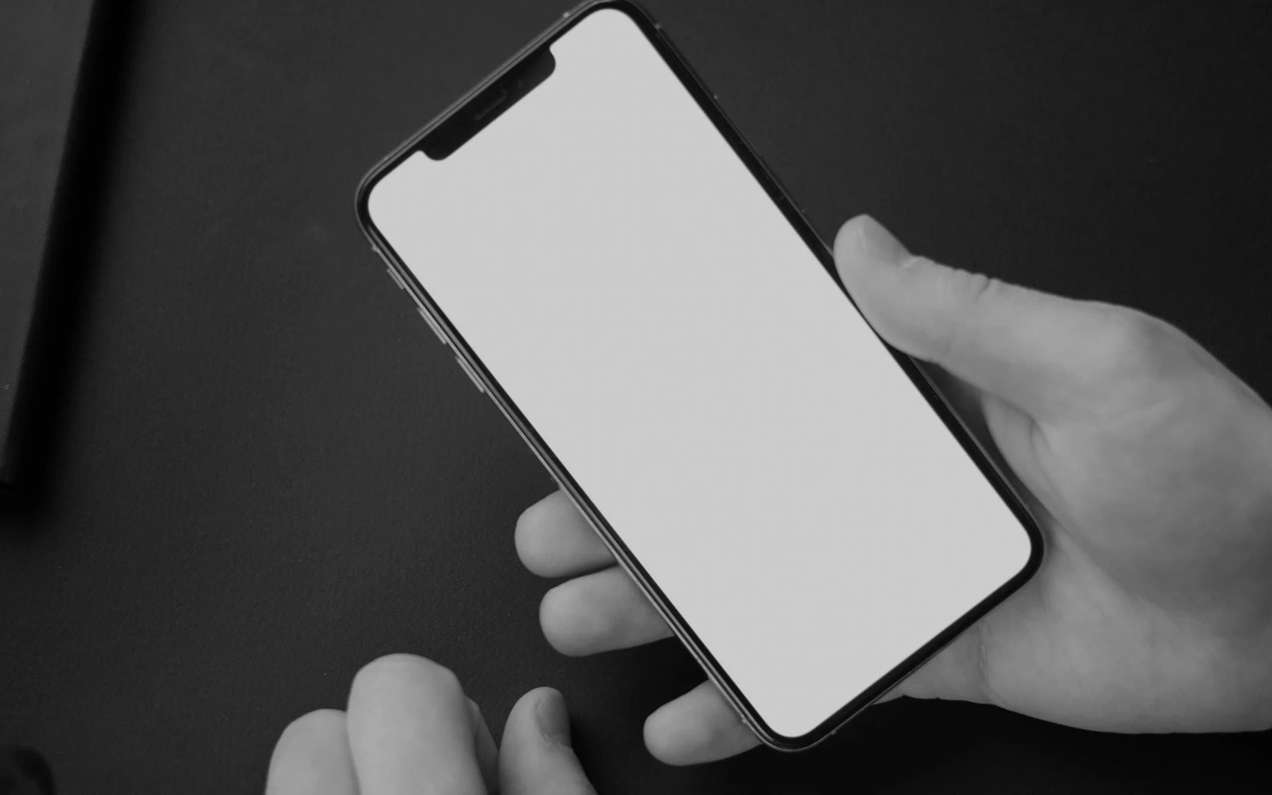 Hands holding a blank illuminated phone over a dark desk